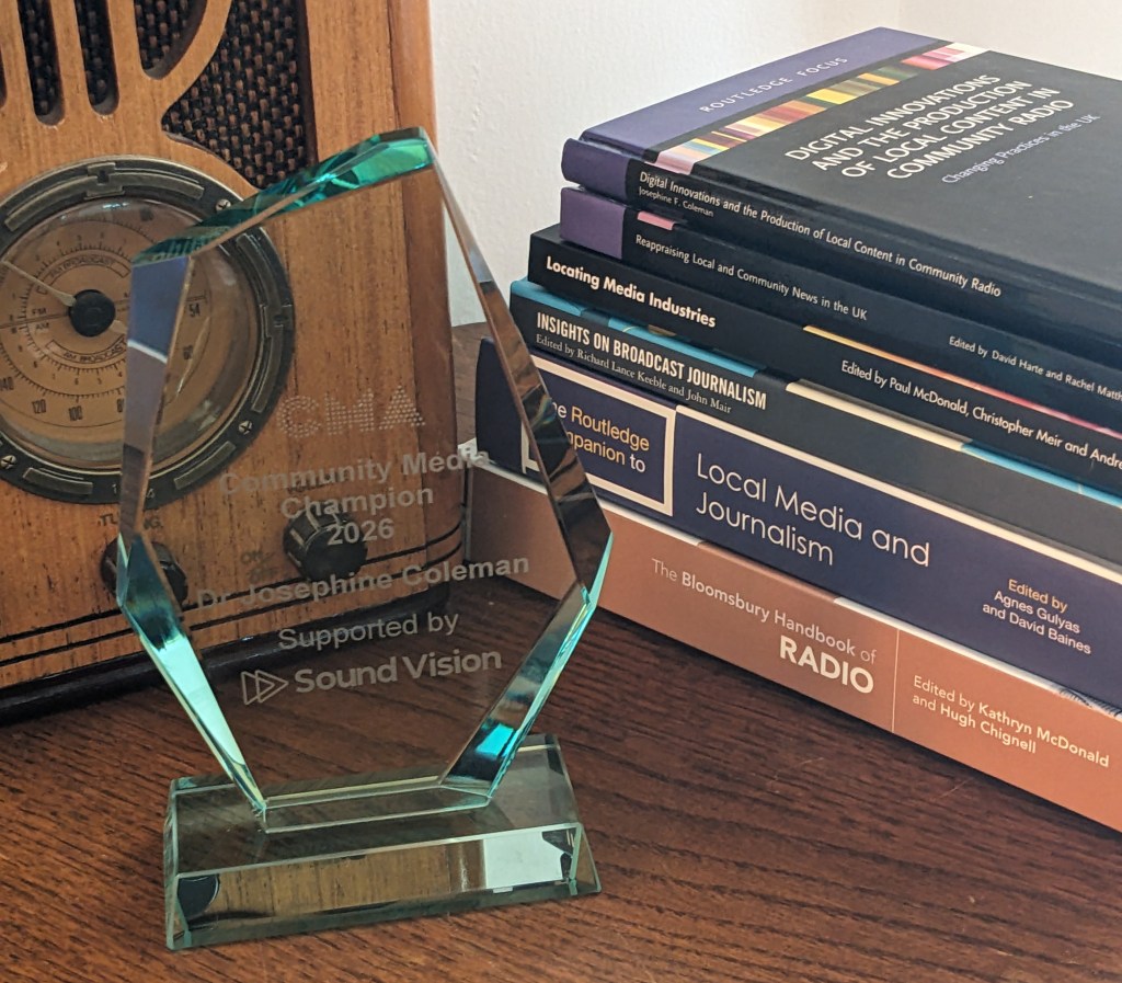 A glass award in front of a wireless and a pile of books